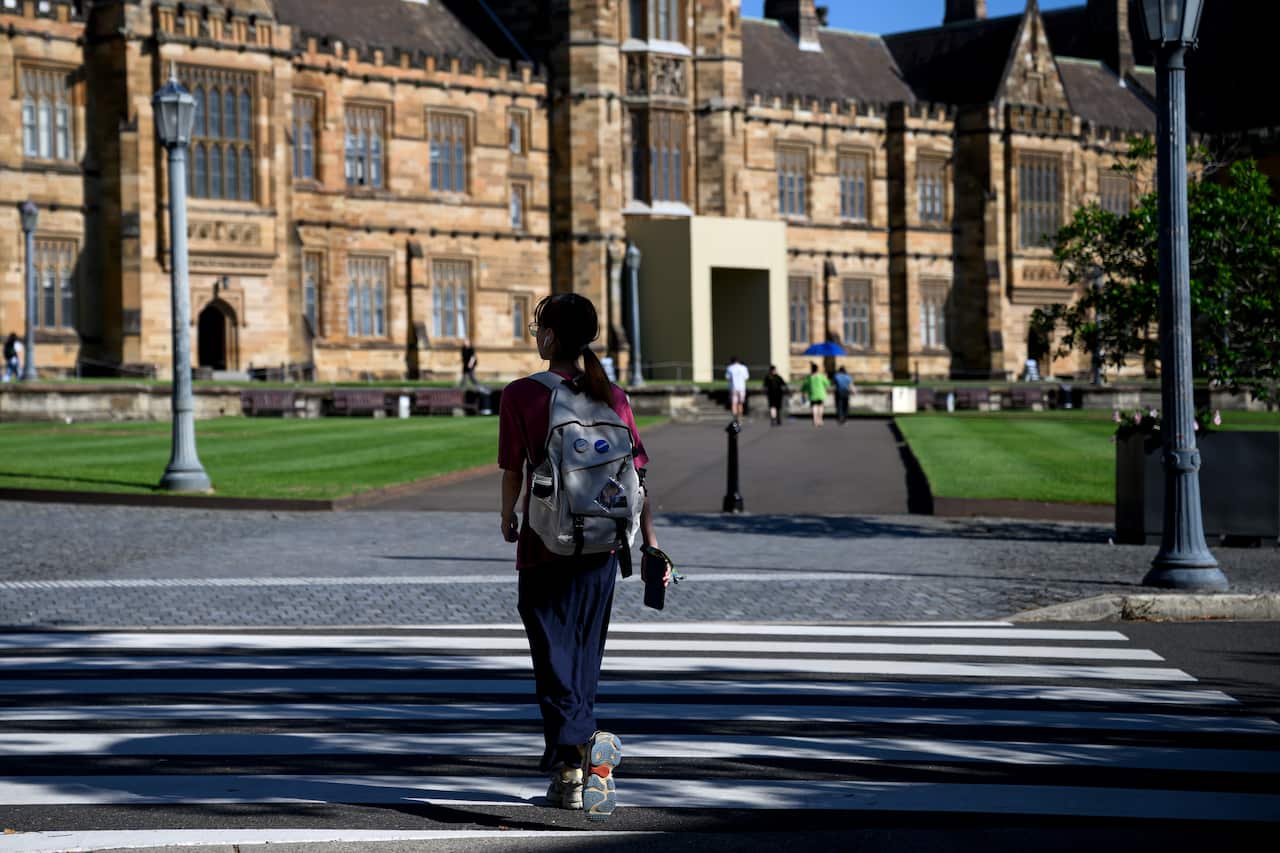 A young woman wearing a backpack walks towards a sandstone building.